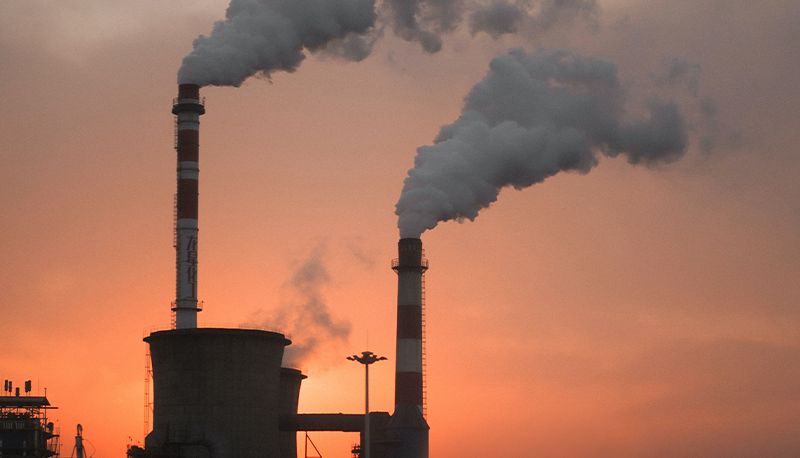 Factory smoke billowing against an orange, sunset sky.