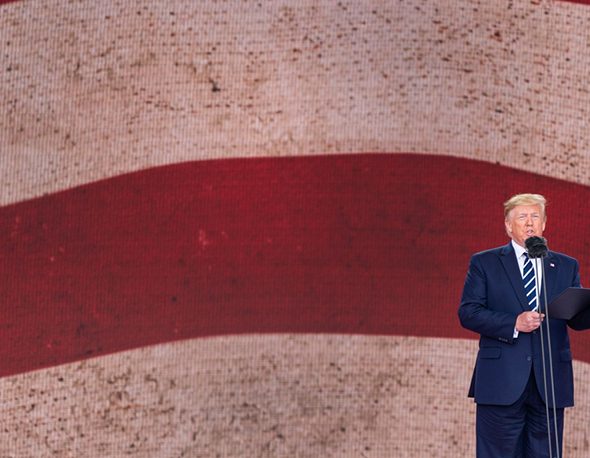 President Donald Trump stands in front of a large wall depicting the American flag