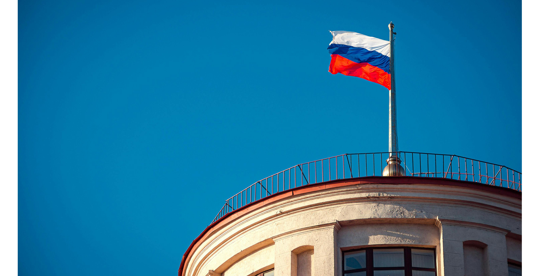 Russian flag flying atop a building in front of a blue sky.